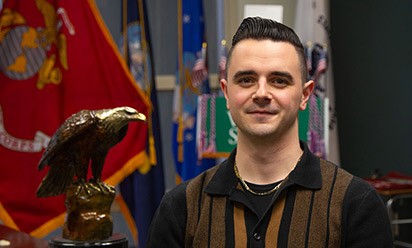 Angelo DePollo next to a golden eagle statue and a Marine Corps flag.