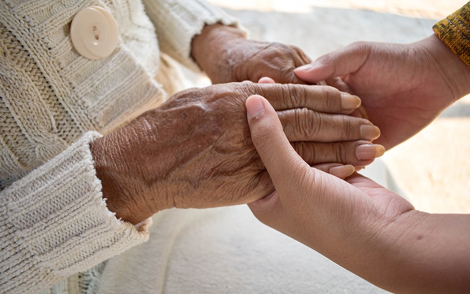 An older person of color's hands are gently held by a younger person's hands.