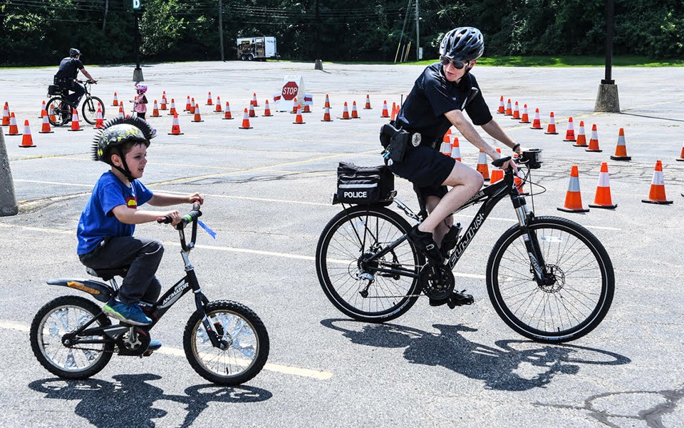 A police officer and a kid wearing a cool bike helmet ride around the parking lot at a Bike Rodeo event.