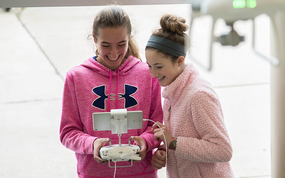 Two young women work the remote control of a drone at the Student Center.