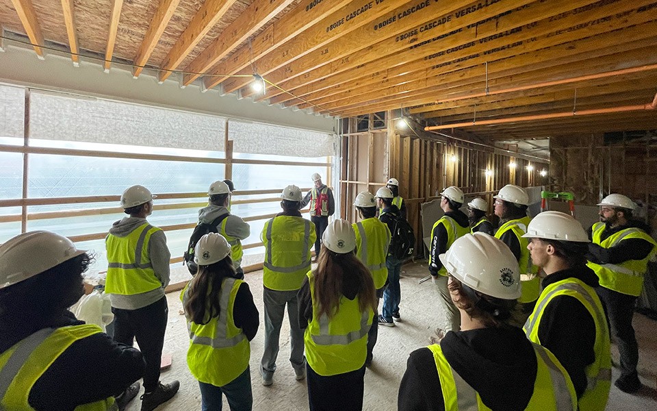 A group of students wearing safety vests and hardhats are given a tour of the Lakeview Apts. construction site.