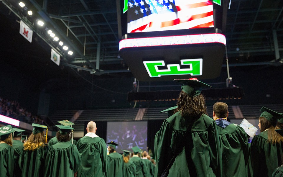 Graduates at an EMU Commencement ceremony with the block E on the the overhead scoreboard at the George Gervin GameAbove Center.