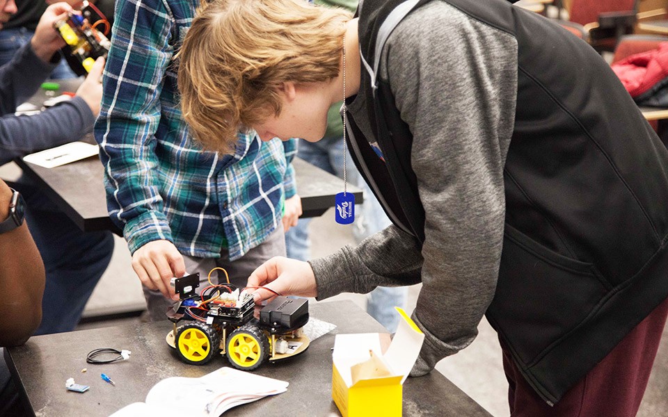 Young men lean over a STEM project at a Digital Dudes event on EMU's campus.