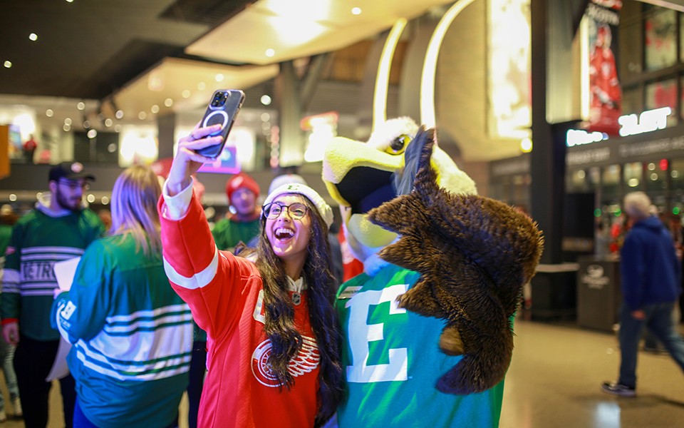 Hockey fan in a Red Wings jersey takes a selfie with Swoop at TRUEMU Night at Little Caesar's Arena