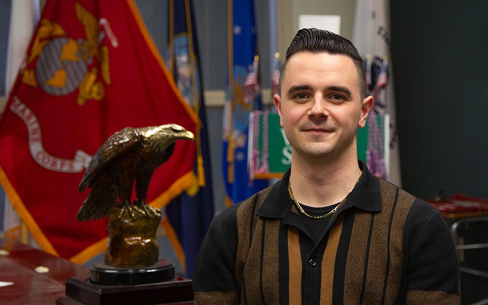 Angelo DePollo next to a golden eagle statue and a Marine Corps flag.