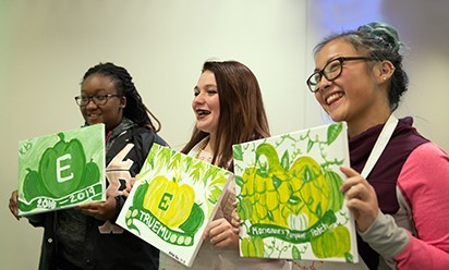 Three students hold up their newly painted canvases.