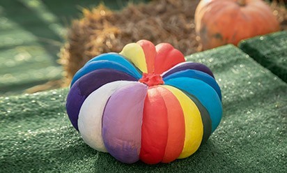 Rainbow painted pumpkin sits among hay bales and gourds