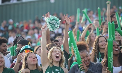 Football fans in the student section smile and wave pompoms