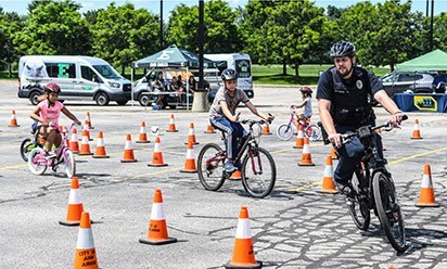 EMU Police officer and kids on bikes ride around orange cones