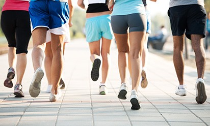 A diverse group of runners and walkers in shorts and running shoes participate in an outdoor event.