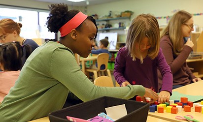 A young teacher works with a pupil building with colorful blocks in a classroom.