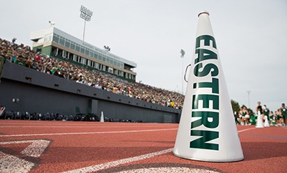 An Eastern megaphone sits on the sidelines of the football field with fans in the stands in the background.