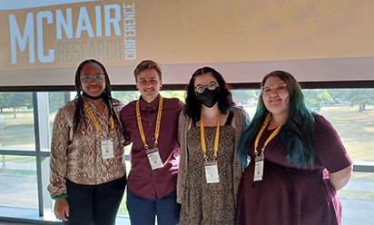 Students Odia Kaba, Ryland Lambert, Coreena Forstner, and Jacklyn Staffeld, in front a McNair Conference projected slide at the 2022 Baylor University McNair Scholars Research Conference.