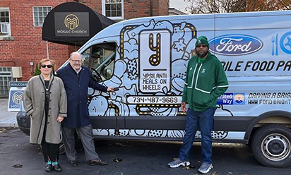 Dr. Connie Ruhl-Smith, President James Smith, and EMU alumnus and former football player Samuel Estes stand by the Ypsilanti Meals on Wheels van, ready to deliver meals.