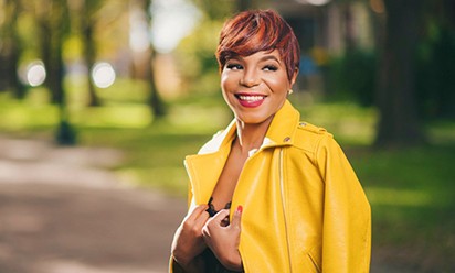Brittni Brown smiles on a tree-lined path with a shiny yellow jacket draped on her shoulders