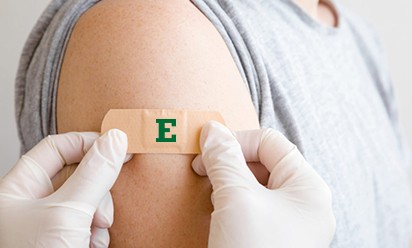 bandaid with green block E being put on right upper arm of person; person holding bandaid is wearing gloves