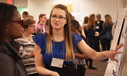 A student presenter explains her research to a symposium attendee.