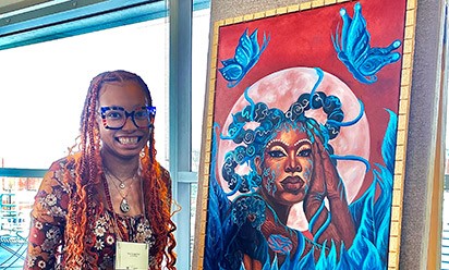 Nia Crutcher stands next to a painting that she's created and is exhibiting in her solo exhibit.