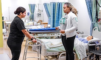 Nursing students work together with a walker, a wheelchair, and medical training manikins.