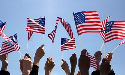 Hands waving small American flags against a blue sky.