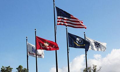 Military flags fly against a blue sky