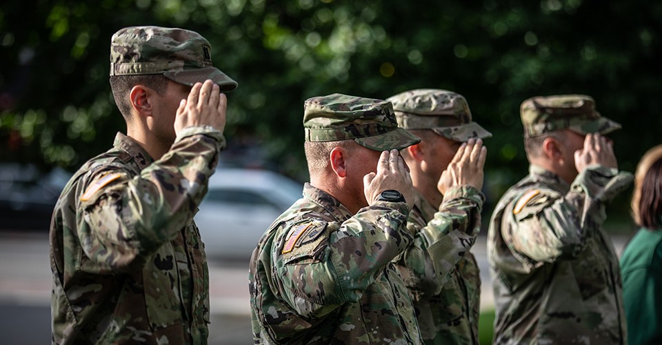 U.S. Army soldiers in camouflage uniforms salute the American flag.