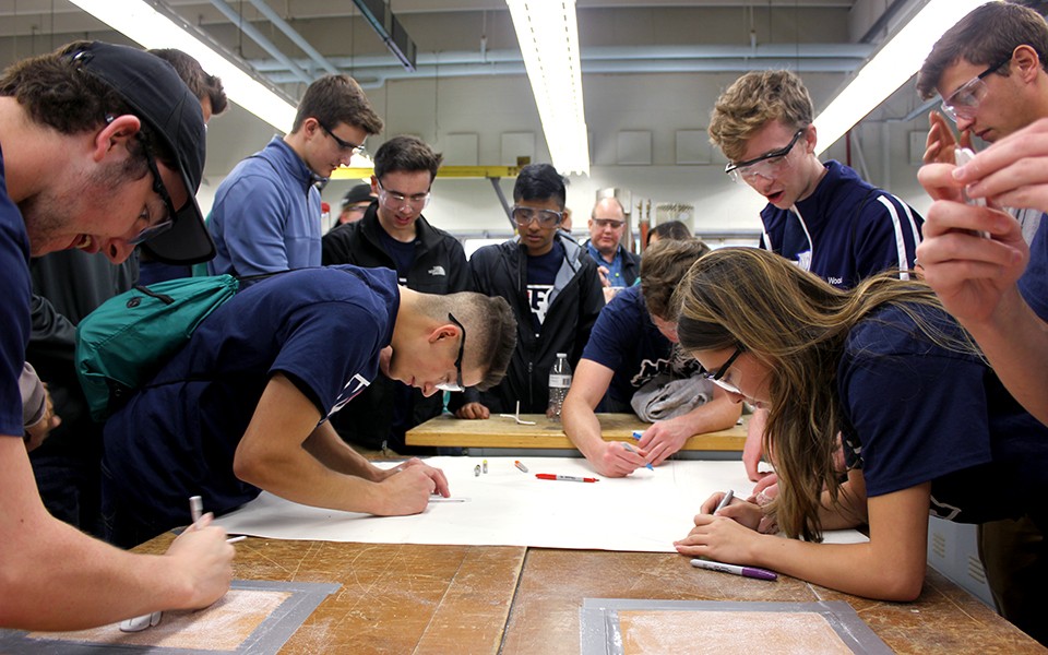 A group of high school student gather around a table drawing on a large piece of paper.