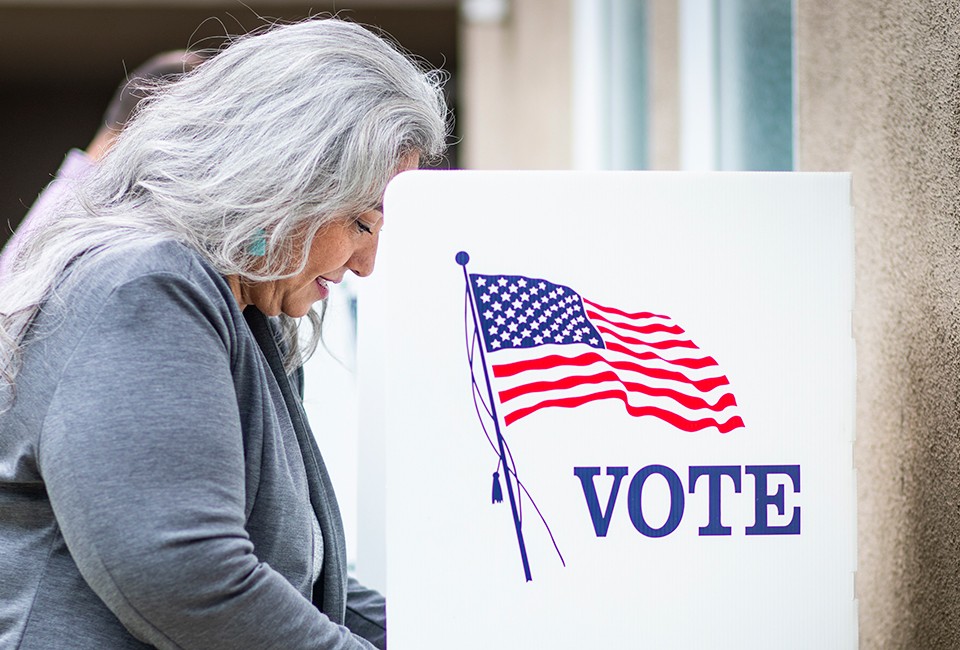 Middle-aged woman in a voting booth marked with American flag and vote sign.