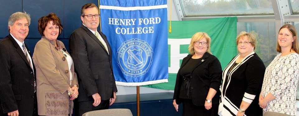 group photo of representatives from Henry Ford College and EMU, with each respective schools' flag in the background