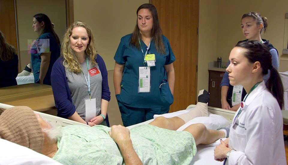 A team of CHHS graduate students gather around the hospital bed of an actor simulating a patient with various health problems.