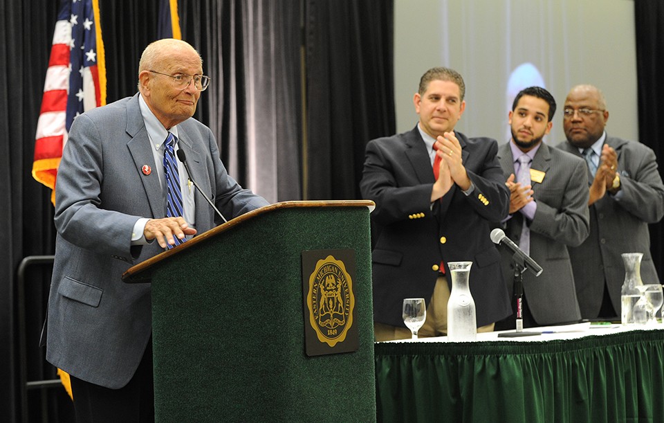 John Dingell speaking at the podium at Eastern Michigan University.