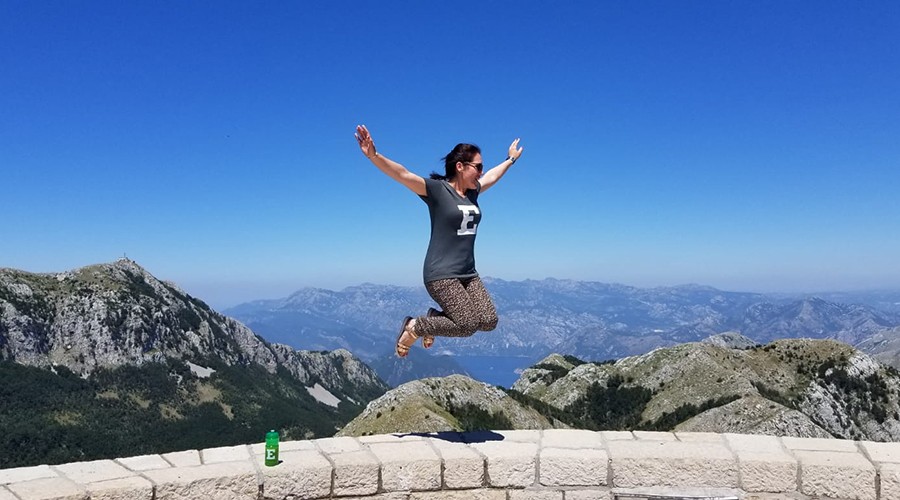 Silvija Marniković wearing EMU shirt jumps at a scenic location in Montenegro