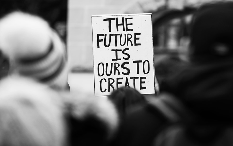 A protest sign reads "The Future is Our to Create"
