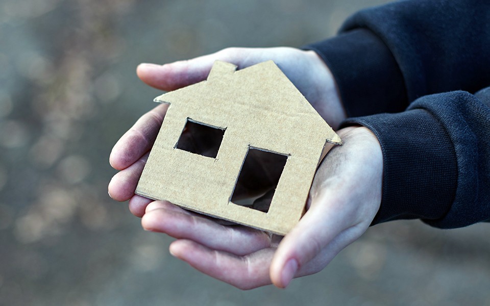Photo illustration of young person's hands holding a cardboard cutout of a house