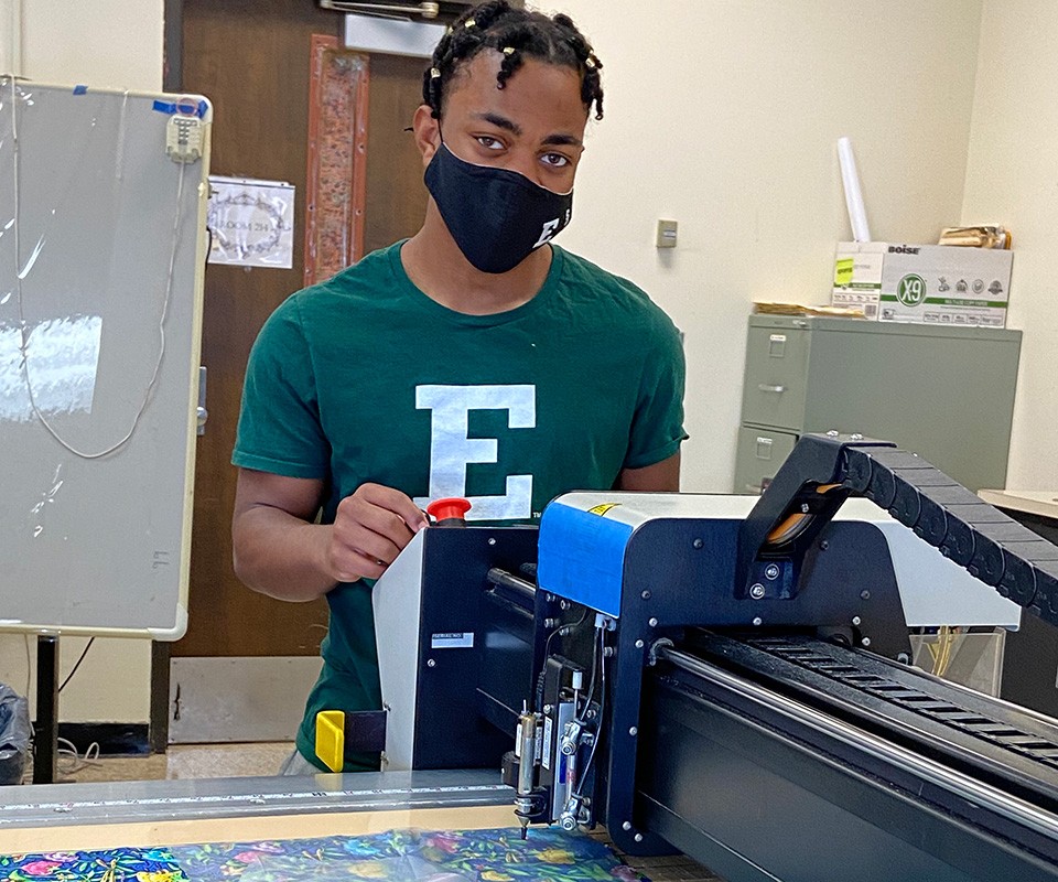 EMU student cutting fabric for quilts on the industrial fabric cutter in the CAD lab.