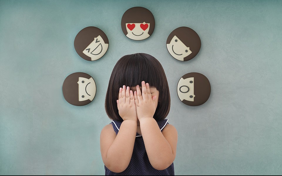 A young girl covers her face and around head are emojis-style expressive faces.