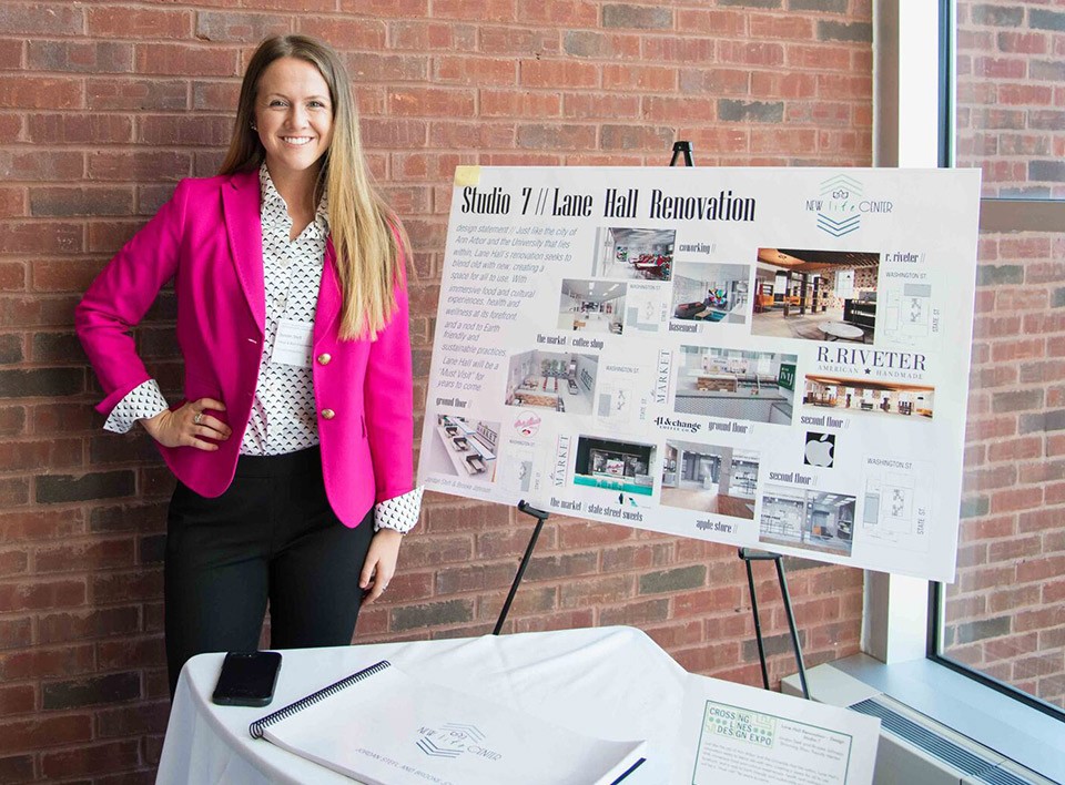 A student stands next to their project display board at a recent Undergraduate Symposium event.