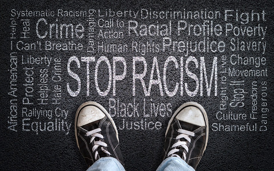 Person wearing tennis shoes and jeans standing over Stop Racism word cloud written on the pavement.