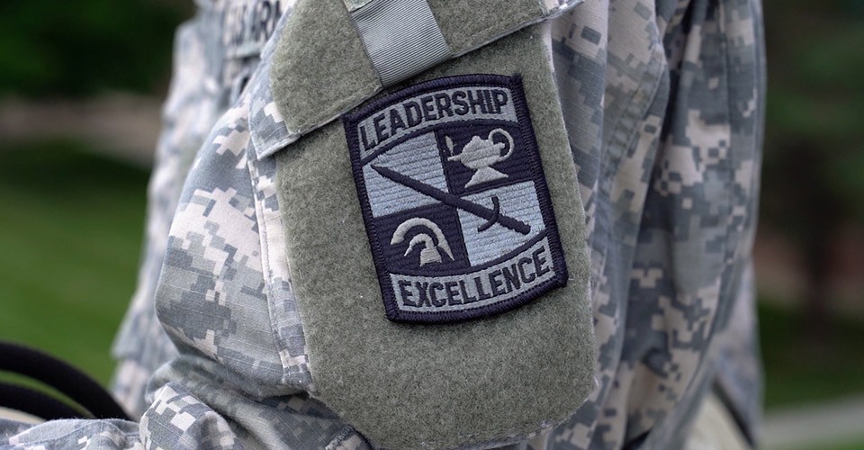 An arm patch on a ROTC camouflage jacket that reads, "Leadership" and "Excellence."