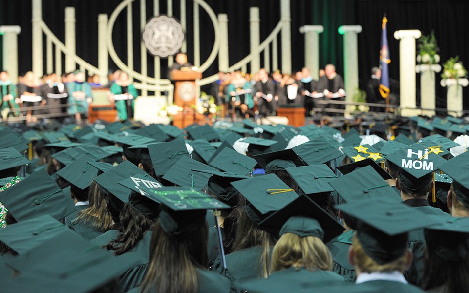 A sea of graduating students in regalia face a speaker on the stage at a commencement ceremony.