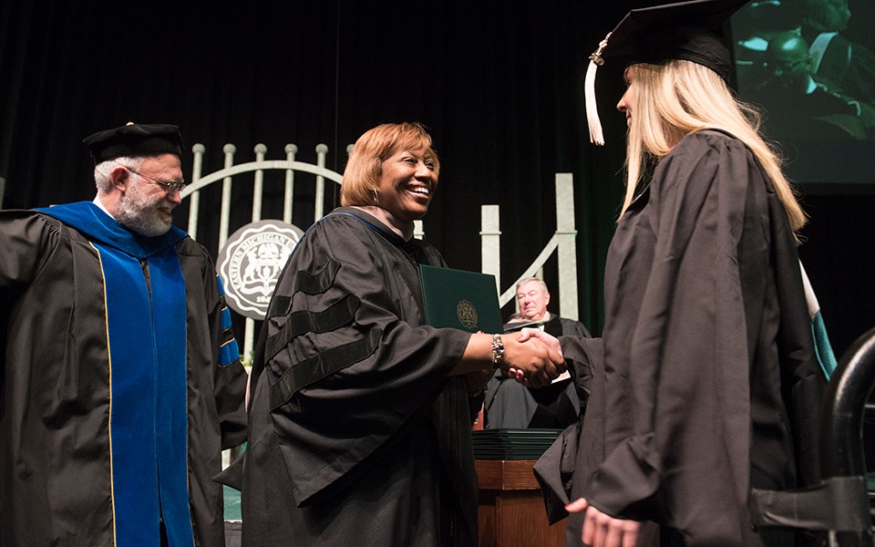 EMU Board of Regents Chair Eunice Jeffries presents a diploma to a graduate at a commencement ceremony.