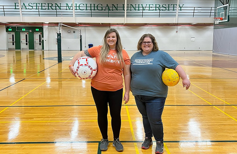 Kara Oliver, left, and Heather Silander, right, are dressed for a therapy session and holding colorful balls in the basketball court at the Rec/IM.
