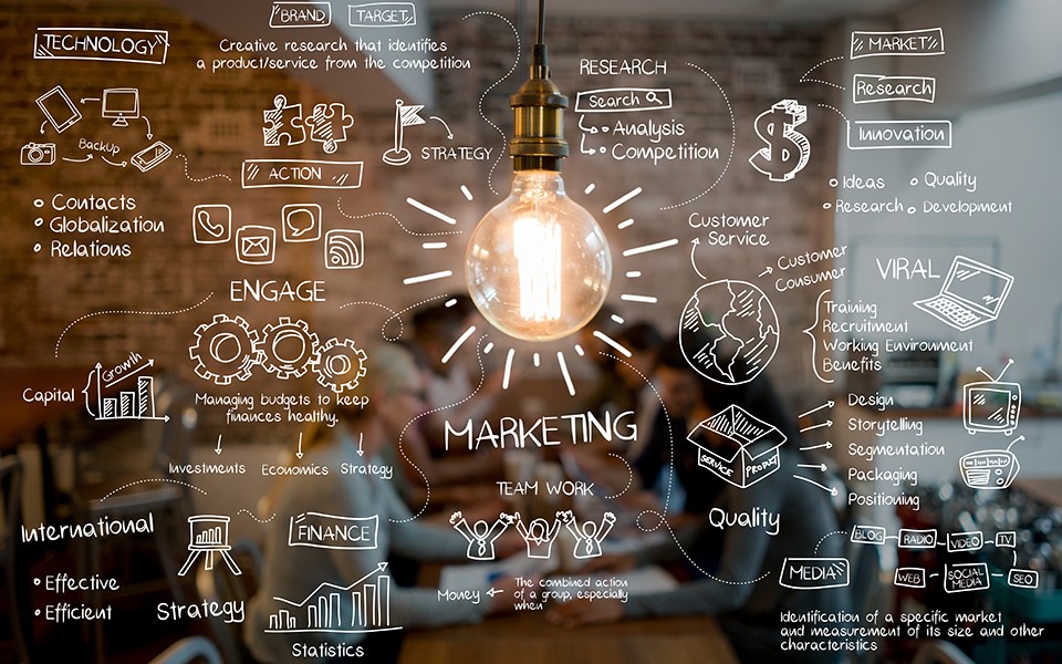A light bulb shines brightly with marketing language written around it, and a team meeting is out of focus in the background.