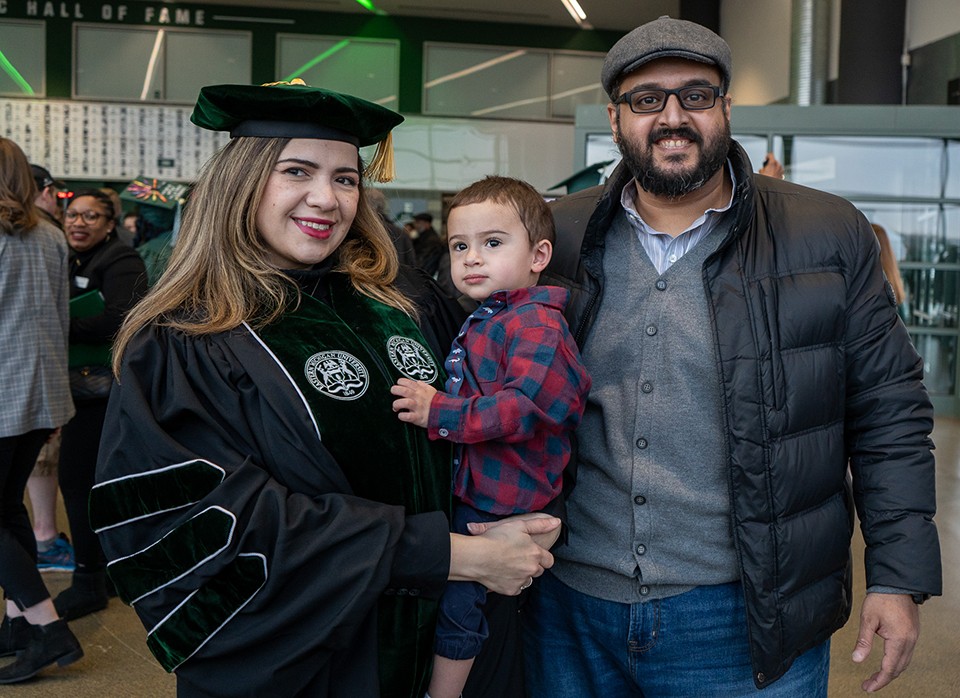 Nadia Arafah,  in her graduation garb and holding her toddler son, is with her husband at the Gervin Center at Winter Commencement.