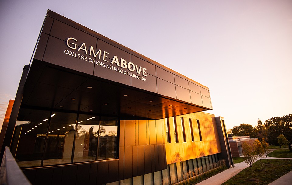 The sign at the renovated GameAbove College of Engineering and Technology is brightly lit by the orange light of the sun.