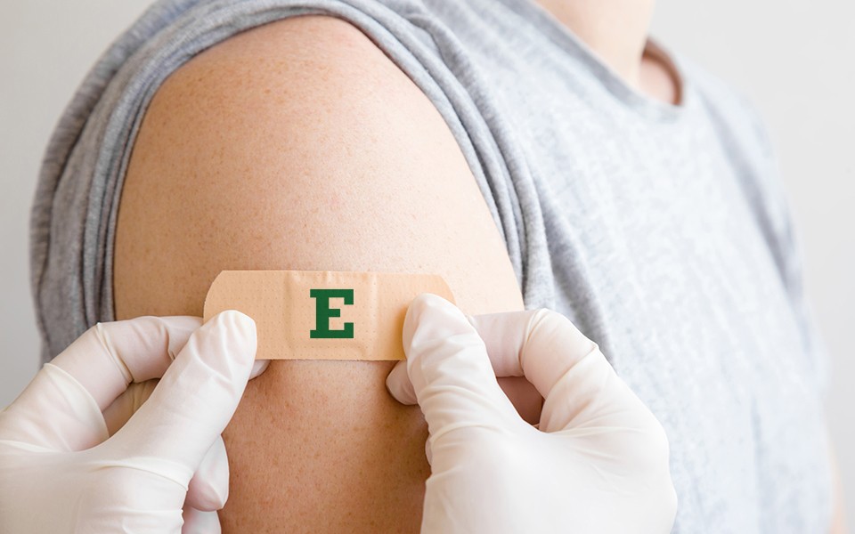 bandaid with green block E being put on right upper arm of person; person holding bandaid is wearing gloves
