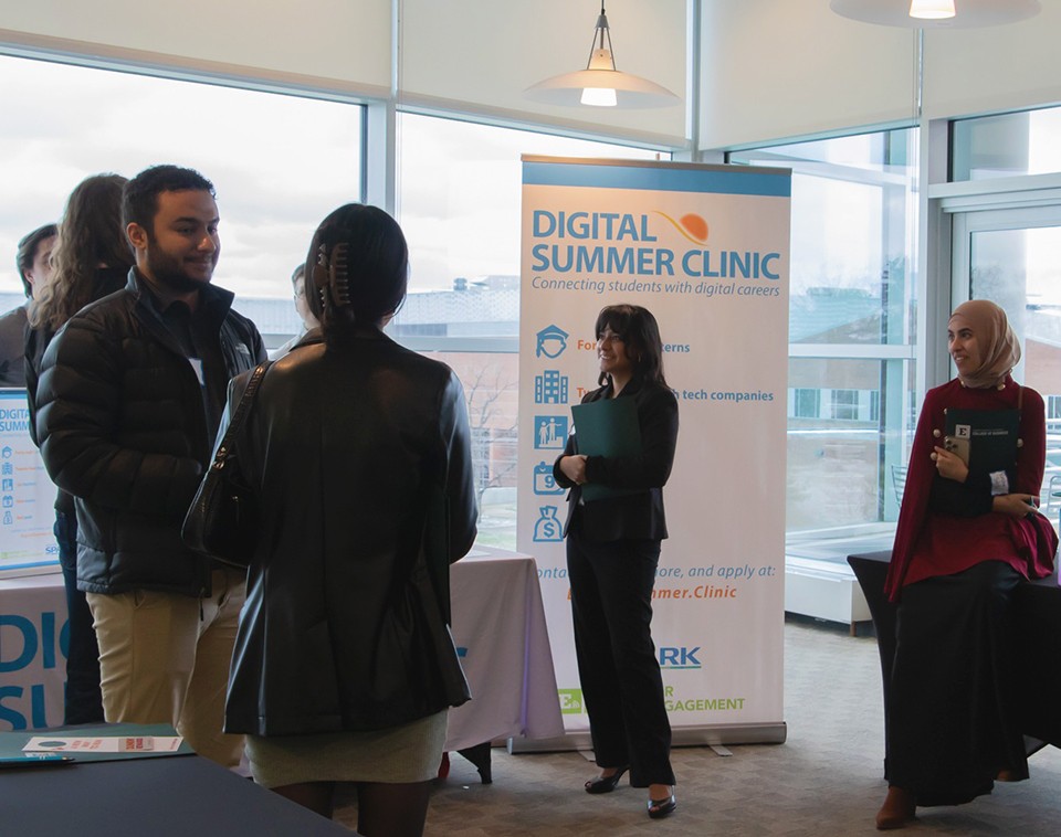 Students chatting in small groups in front of the Digital Summer Clinic banner.