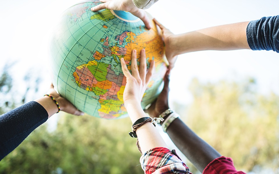 A diverse group of young people's hands holding up a globe outside