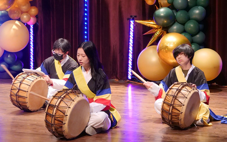 Performers in the Colors in Harmony cultural talent show play drums while seated on the stage