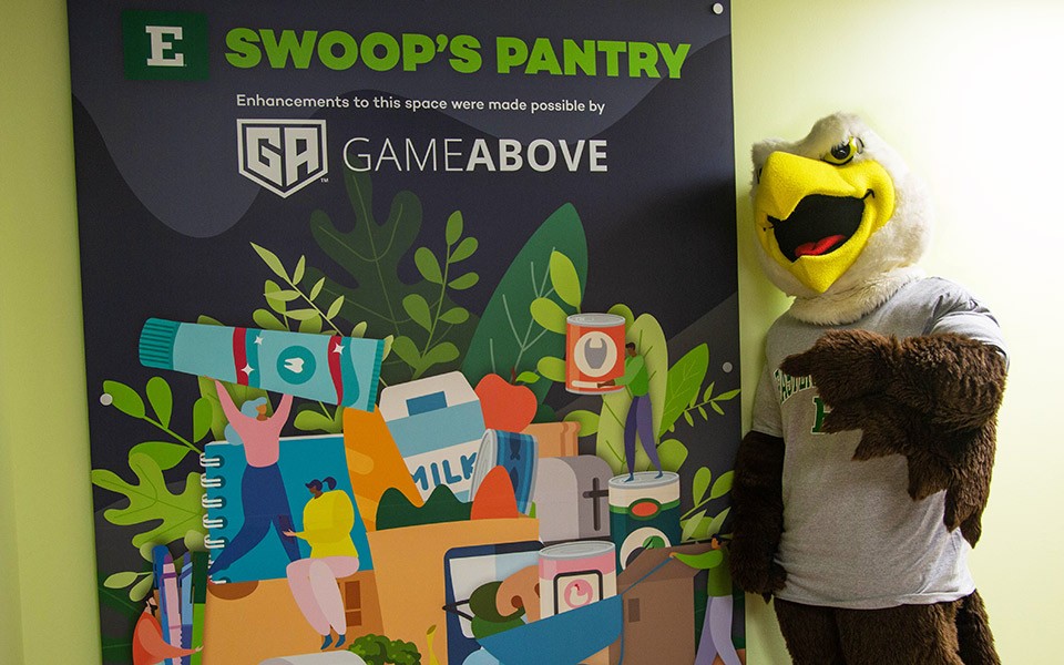 Swoop stands by a color banner for the food pantry that features the GameAbove logo